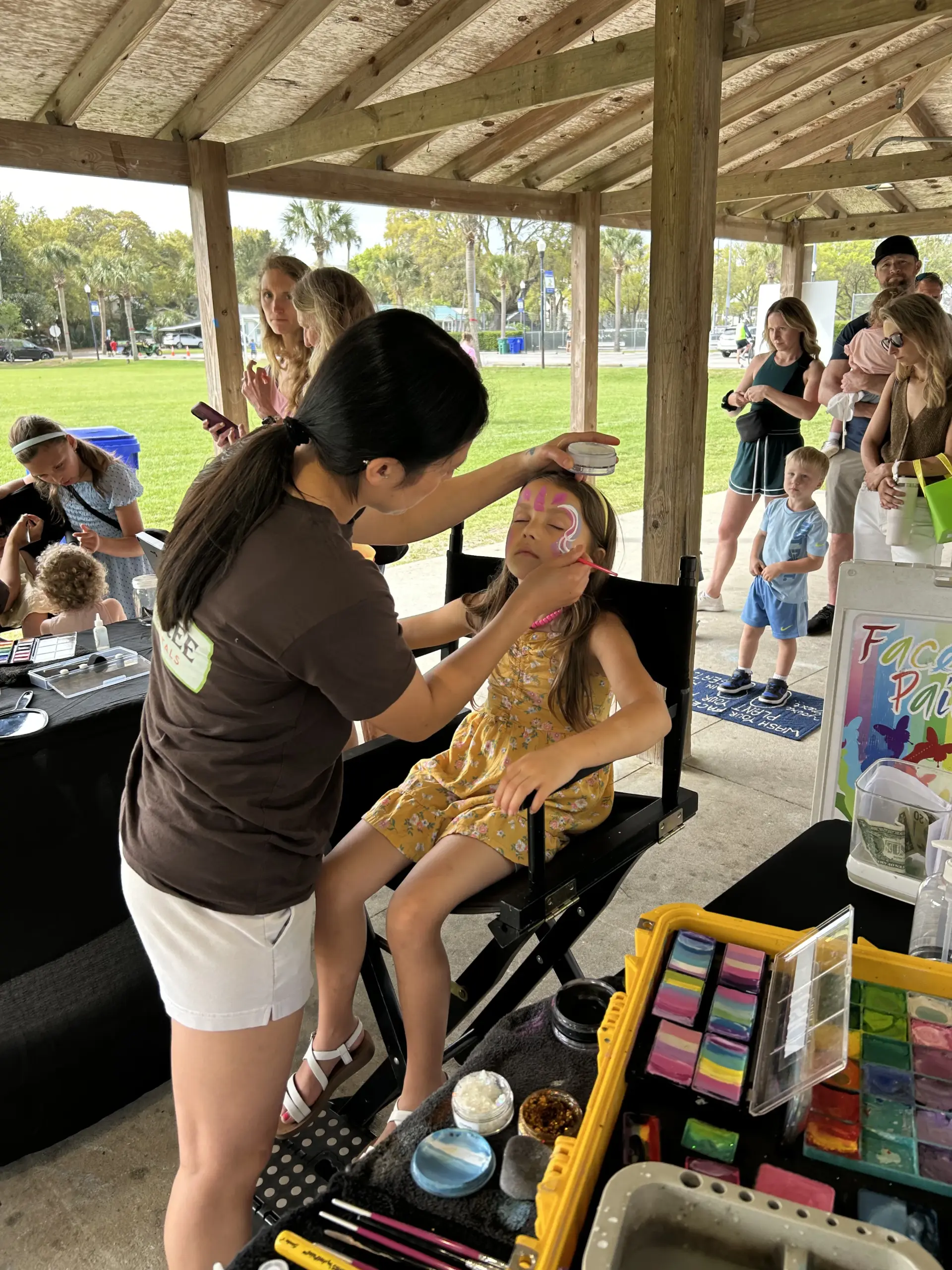 Professional face painter from Palm Tree Party Rentals applying colorful design to a young girl's